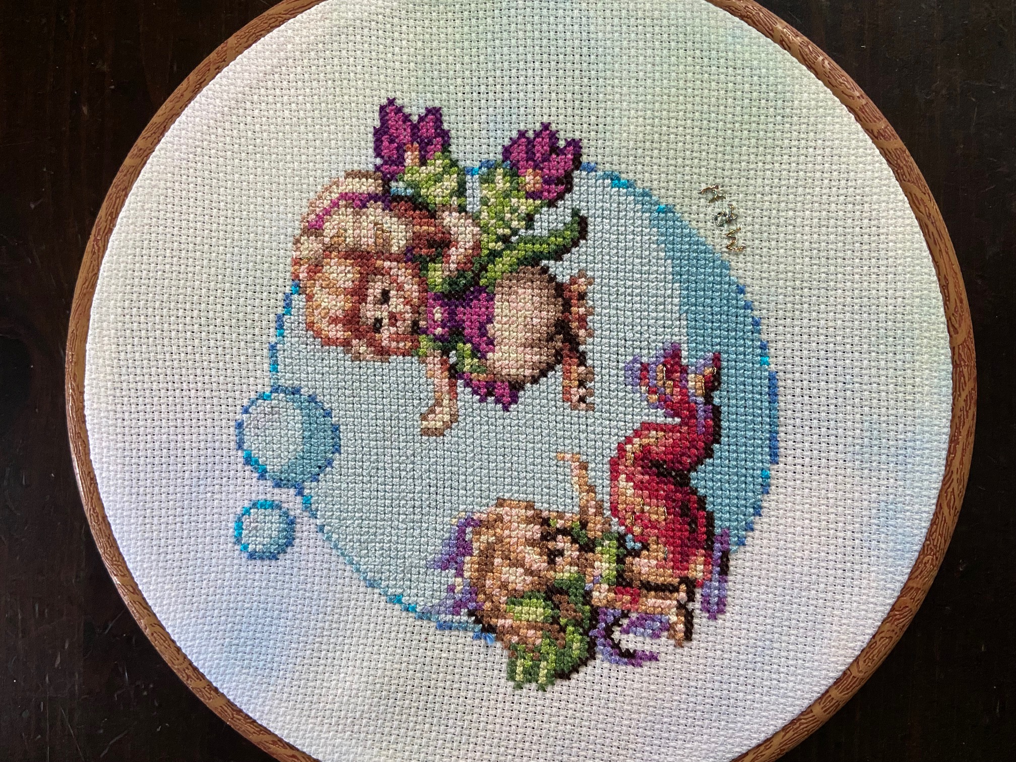 A cross stich in a hoop of a mermaid and a siren video game sprites from Legend of Mana.